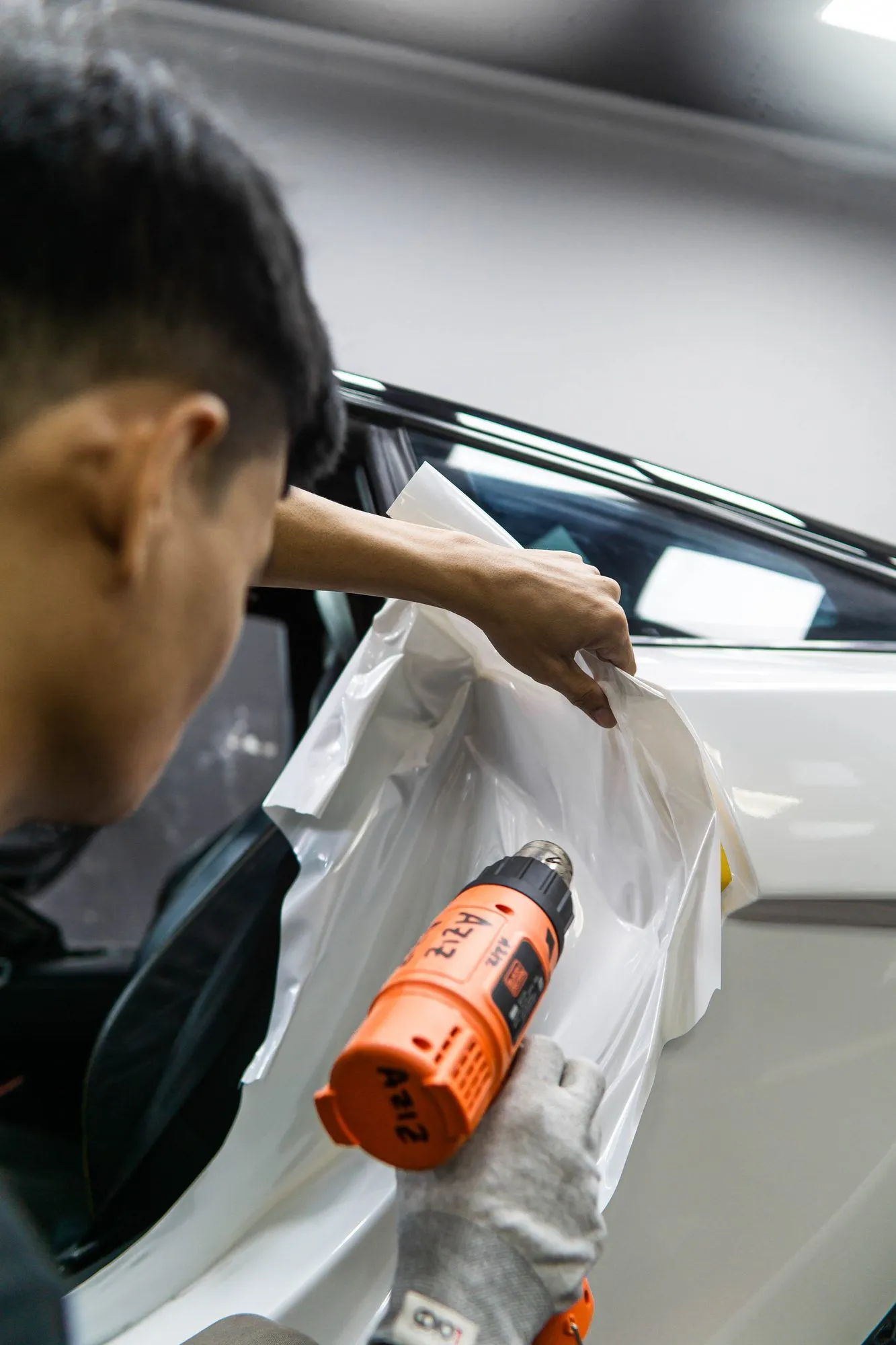 Teknisi memanaskan film wrapping putih dengan heat gun