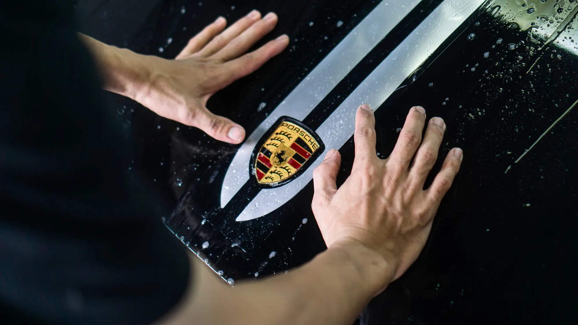 Tangan teknisi meratakan film di kap Porsche dekat emblem